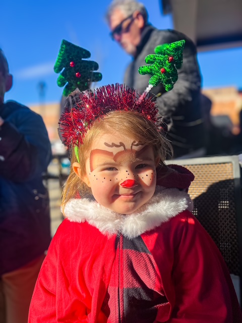 A small child in a Christmas cape with a reindeer design painted on her face