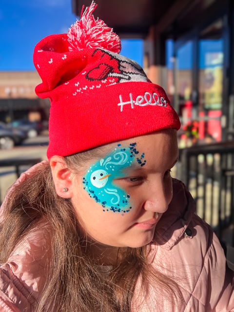 A girl with a Christmas hat and snowman face painting by Face Painters NH