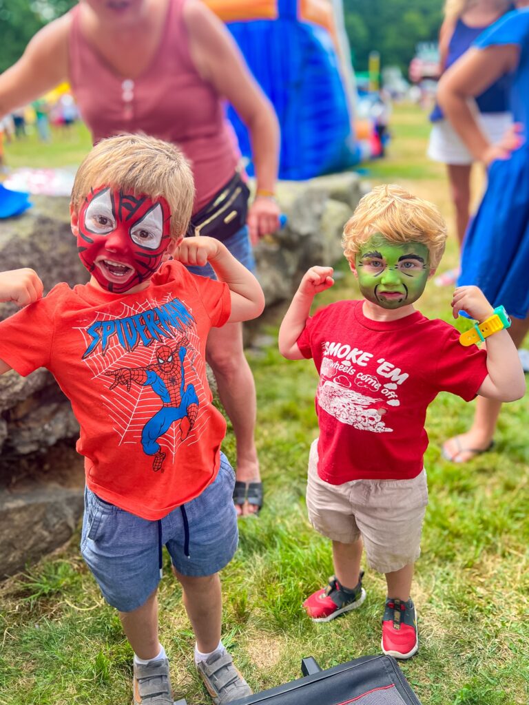 Two boys with Spider Man and Hulk face paint flexing muscles like super heroes