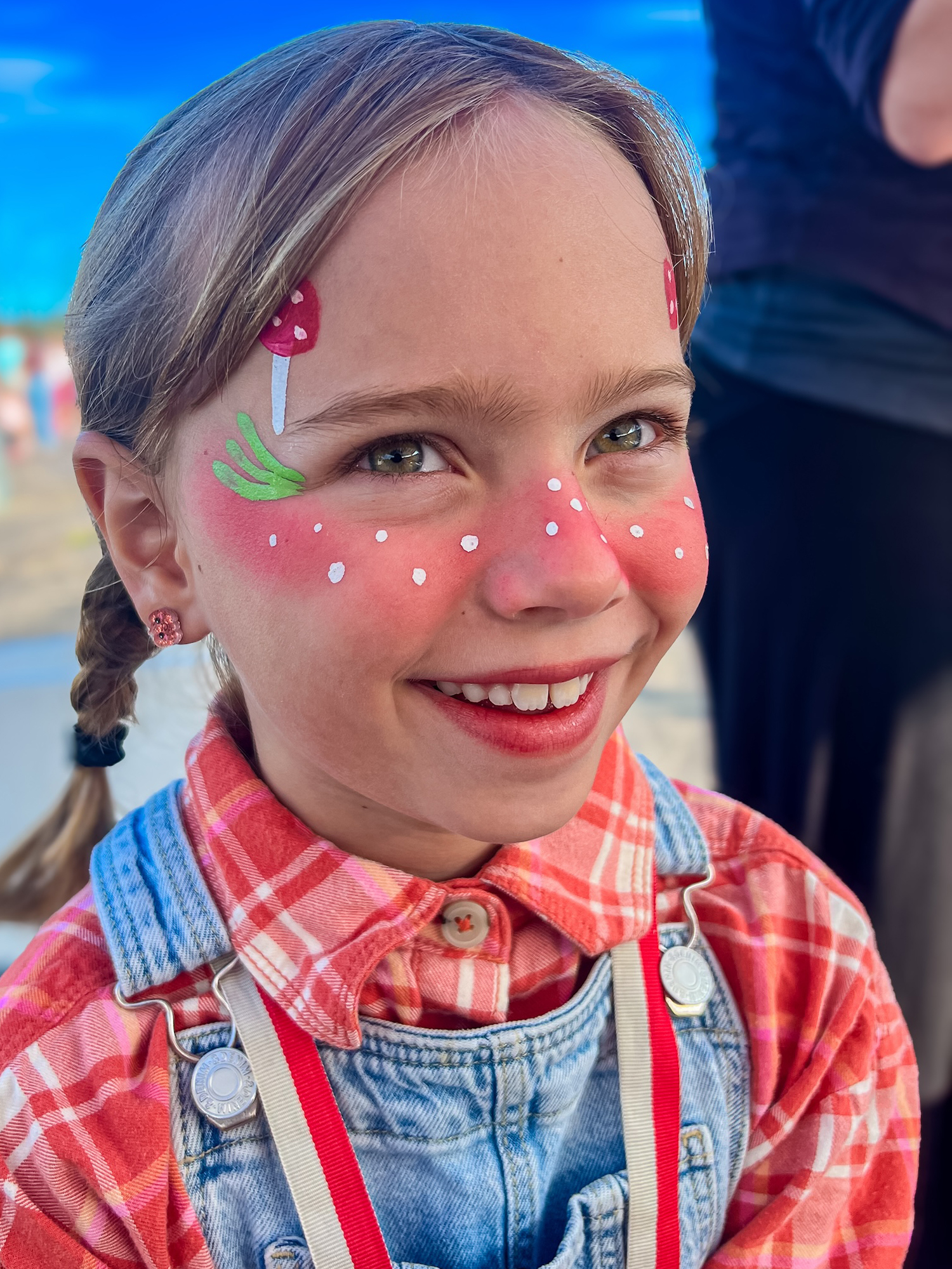 A girl in overalls and a flannel shirt with a mushroom fairy face painting